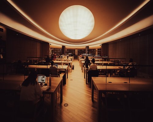 A person adjusting the display brightness of a smartphone to match the gentle indirect lighting of a cafeteria room